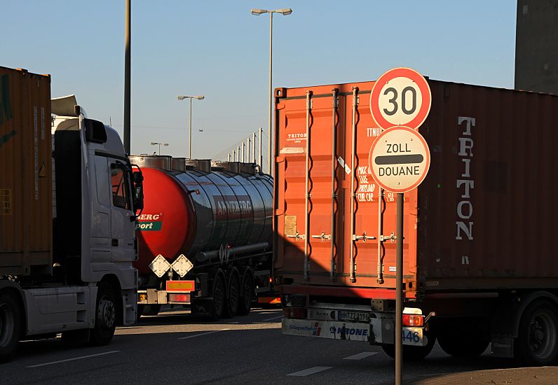 017_19021 Lastwagen mit Containern und ein Tanklastzug warten am Zoll auf ihre Abfertigung - ein Strassenschild mit der Aufschrift Zoll / Douane sowie der Geschwindigkeitsbegrenzugn auf 30 km/h. Fotograf hamburg  www.christoph-bellin.de