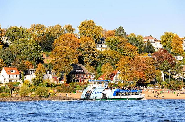 1015_154  Eine Hafenfhre fhrt zum Anleger Oevelgnne / Neumhlen; am Elbstrand sitzen Menschen in der Herbstsonne und blicken auf die Elbe. Die Bume zwischen den Husern zeigen prchtige Herbstfarben.  