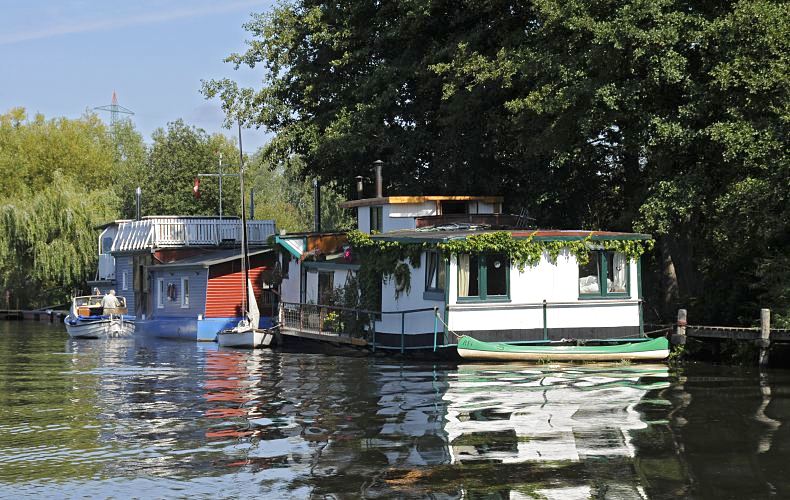 Mehrere Hausboote liegen am Ufer der Doveelbe in Hamburg Reitbrook. Die schwimmenden Huser spiegeln sich in dem ruhigen Wasser der Dove-Elbe. Ein Kanu, Segelboot und ein Motorboot sind an den Hausbooten festgemacht.  Sommerbilder aus Hamburg Bergedorf - Hausboote auf der Dove-Elbe bei Reitbrook