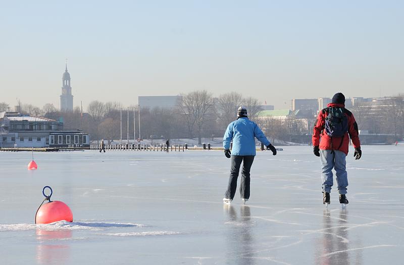 42_5592 Ein Paar nutzt den sonnigen Wintertag und luft Schlittschuh auf der Aussenalster - die Bojen vor einer Segelschule sind im dicken Eis festgefroren. Hamburg im Winter - Eislaufen auf der zugefrorenen Aussenalster.