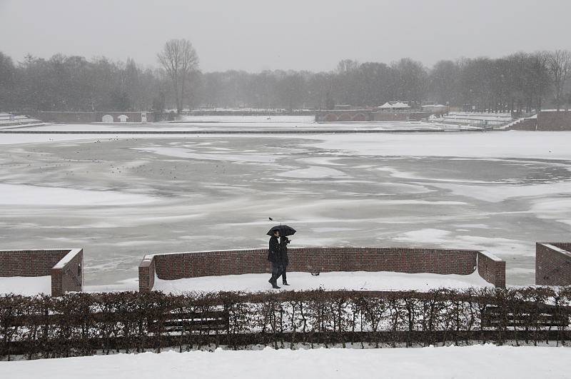68_5042 An einem grauen Wintertag geht ein Paar am Stadtparksee spazieren - sie schtzen sich miti einem Schirm gegen den Schneefall. Auf dem fast zugefrorenen See sitzen Mwen auf dem dnnen Eis. Im Hintergrund das Freibad Stadtparksee. Fotos von Hamburg im Winter - Grauer Wintertag am Stadtparksee, Spaziergnger.
