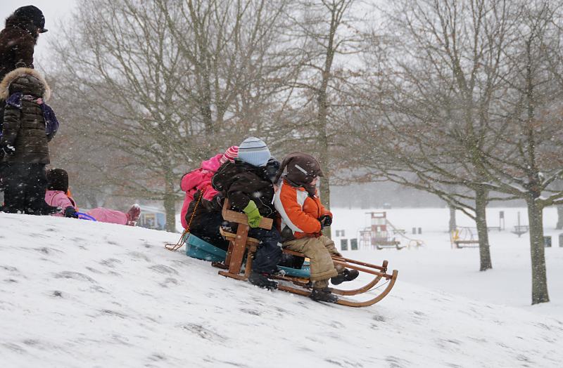 69_5027 Im dichten Schneetreiben lassen sich die Kinder ihren Spass nicht nehmen, einen kleinen Hgel im Hamburger Stadtpark herunter zu rodeln. Im Hintergrund der Spielplatz und das eingeschneite Planschbecken. Fotos von Hamburg im Winter - Kinder fahren Schlitten im Stadtpark.