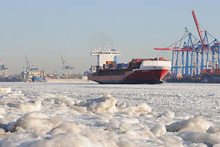 02_5775 Zwei Frachtschiffe verlassen im dichten Eis der Elbe den Hamburger Hafen - rechts die Container - Brücken am HHLA Terminal Burchardkai. Im Vordergrund ist der Elbstrand von Övelgönne mit Eisschollen bedeckt