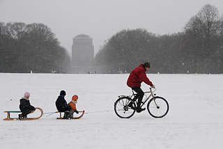 64_5069 Der Hamburger Stadtpark ist eingeschneit. Ein Vater zieht mit seinem Fahrrad die zwei Schlitten seiner Kinder durch den Schnee ber die groe Wiese. Bilder vom Winter in der Hansestadt Hamburg - Winterfreuden im Hamburger Stadtpark. 