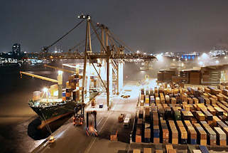 011_15288 ein Containerschiff liegt am Kai des Container Terminals Burchard, auf der anderen Seite der Elbe die beleuchteten Häuser von Hamburg Neumühlen. Containercarrier transportieren die Container auf die Lagerfläche, auf der die Metallboxen in dichten Reihen  gestapelt sind. Der Hamburger Hafen liegt mit z. Zt. 8.1 Mio TEU weltweit auf Platz acht der Containerhäfen. TEU = Container, die 20 Fuß Länge (6,096 m) + die Breite von 8 Fuß ( 2,44 m) haben; (Twenty-foot Equivalent Unit)
