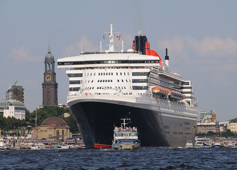 Hamburgfotos - Bilder von der Queen Mary 2 auf der Elbe - Hamburger Michaeliskirche  011_59_4382 Die Queen Mary 2 auf der Elbe vor den St. Pauli Landungsbrücken; lks. die Kuppel vom Eingangsgebäude des Alten Elbtunnels, dahinter der hohe Kirchturm des Hamburger Michels und rechts die schwedische Gustav-Adolf-Kirche.  Viele Barkassen, Schiffe der Hafenrundfahrt und private Sportboote /  Motorboote begleiten den gewaltigen Luxusliner bei  seiner Fahrt auf der Elbe; auch an den Landungsbrücken stehen die Schaulustigen dicht gedrängt.  ©www.hamburg-fotograf.com