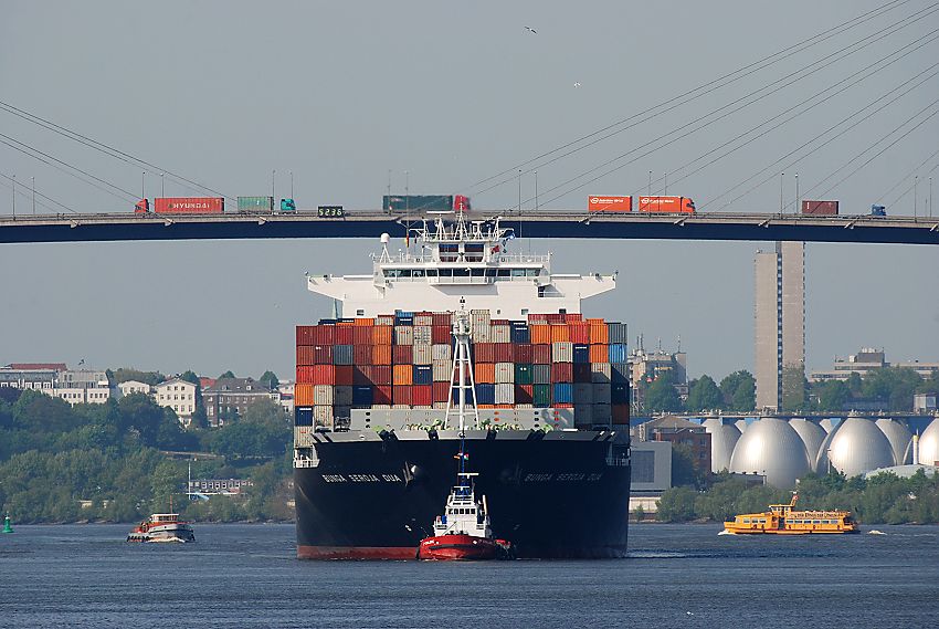 011_15572 ein vollbeladenes Containerschiff luft in den Hamburger Hafen ein; ein Schlepper untersttzt den Containerriesen in der Steuerung am Schiffsbug.Auf der Khlbrandbrcke werden die Container per Lastwagen an ihren Bestimmungsort transportiert - rechts fhrt eine HADAG Fhre auf der Elbe Richtung Finkenwerder. www.christoph-bellin.de