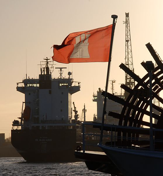 011_32795/00 die Hamburg Flagge weht im Wind am Heck eines Raddampfers der Hamburger Hafenrundfahrt. Im Hintergrund wird ein Frachter am Kai mit einem Kran gelscht.   www.fotograf-hamburg.de