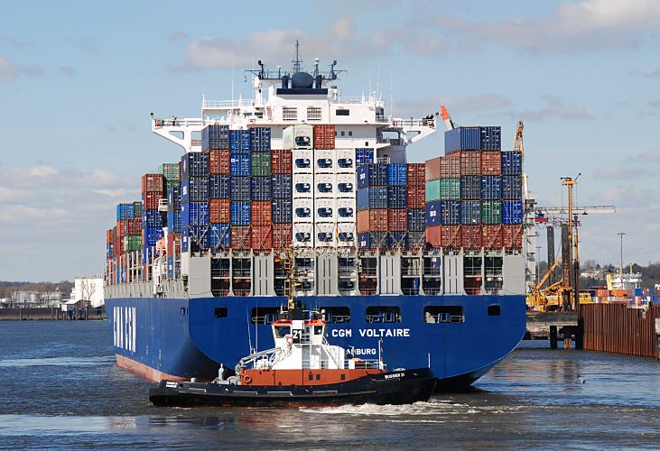 011_26054  der Containerfrachter CMA CGM VOLTAIRE wird von den Hafenschleppern der Hambuger BUGSIER Reederei in das Hafenbecken des Waltershofer Hafens  gezogen, damit das Frachtschiff dann aus eigener Kraft auf der Elbe Richtung Nordsee fahren kann. Die Container sind hoch auf mehreren Ebenen auf dem Deck des Schiffs gestapelt - am Heck steht der Name des Frachtschiffs und der Heimathafen Hamburg.    www.christoph-bellin.de