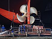 011_22118/00 im Trockendock der Schiffswerft Blohm + Voss bekommt ein Frachtschiff eine neue Schiffsschraube aus glänzendem Messing - Hafenarbeiter reinigen die Werftanlage  mit einem Wasserstrahl.