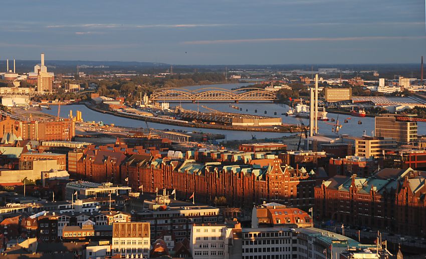 017_18926 Hamburg im Licht vom Sonnenuntergang - der rote Backstein der Speicherstadt leuchtet in der Abendsonne. In der linken Bildmitte verluft der Baakenhafen, an dessen vorderer Kaianlage die Bauarbeiten fr die Hamburger Architektur - Universitt / HafenCity Universitt Hamburg (HCU) begonnen haben. Im Hintergrund die Bgen der Elbbrcke ber die Norderelbe.