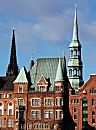 017_18931 Trme der Hansestadt Hamburg; links der Kirchturm der St. Nikolaikirche an der Willy-Brandt-Strasse, deren Ruine als Mahnmal an die Opfer des II. Weltkrieg gedenken soll. Rechts der Kirchturm der Hauptkirche St. Katharinen. Im Vordergrund Giebelturm und Erker des Klinkergebudes am Sandtorkai.