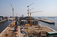 017_18968 Blick ber die Baustelle am Kaiserkai; die Bauarbeiten am Kaiserkai sind fortgeschritten, Baukrne ragen in den blauen Hamburger Himmel. Zwei Besucher mit Bauhelm blicken interessiert auf das Areal der zuknftigen Hafencity zwischen Sandtorhafen und Grasbrookhafen.