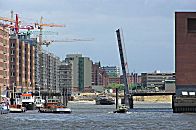 017_18975 Blick in den Sandtorhafen (2004); die Sandtorhafenbrcke ist hochgeklappt, ein Schiff fhrt aus dem Sandtorhafen zur Elbe; die Bauarbeiten am Sandtorkai sind in vollem Gange, die Baukrne stehen dicht gedrngt auf den Baustellen. Es wird am Ende des Hafenbeckens begonnen, Sand fr die zuknftigen Magellanterrassen aufzuschtten - vor dem historischen Gebude des Kaispeicher B steht noch das Gebude der Kaffeelagerei, das der Entstehung der Hafencity 2007 weichen musste. 