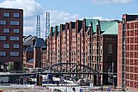 017_18979 die Bebauung der Strasse "Am Sandtorkai" in der Hamburger Speicherstadt ist geprgt durch die historischen Backsteinspeicher und die moderne Architektur der Hafencity. Im Vordergrund die Kibbelstegbrcke, dahinter symbolisieren das runde hohe Eisengerst die ehemaligen Schornsteine vom Kesselhaus. 