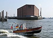 017_18996 ein schnelles Motorboot der Hamburger Feuerwehr verlsst seinen Standort am Kehrwieder und fhrt in rasanter Gleitfahrt auf die Elbe - im Heck des Boots wehen die Hamburg-Fahne und die "Nationale" / Deutschlandflagge im Fahrtwind. Im Hintergrund die massive Speicherarchitektur des Kaispeichers A.  www.christoph-bellin.de