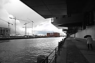 017_18999 Hamburger Regenwetter, ein Hamburg Tourist geht mit Regenschirm entlang der Promenade am Sandtorkai / Sandtorhafen in der Hafencity - links die hohen Baukrne am Kaiserkai. Im Hintergrund der Kaispeicher A, der mit einem Glasaufbau versehen das neue Wahrzeichen Hamburgs, die Elbphilharmonie, werden soll.