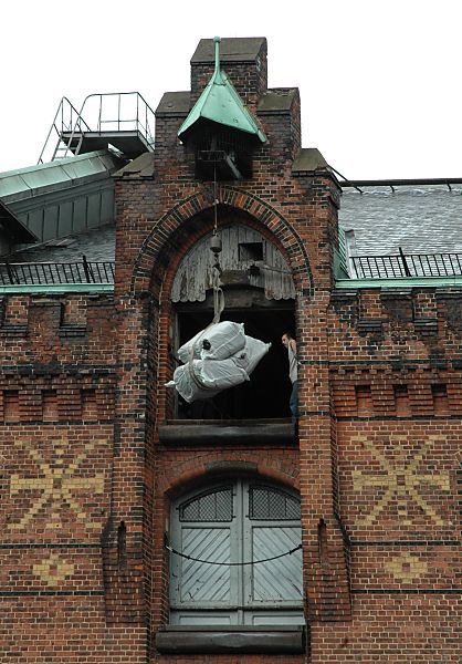 017_18954 mit der Winde werden die Ballen auf den obersten Boden des Speichers gebracht und von einem Lagerarbeiter entgegen genommen. In der Klinkerfassade des Speichergebudes sind mit hellen Klinkersteinen Dekorelemente eingelassen. www.christoph-bellin.de