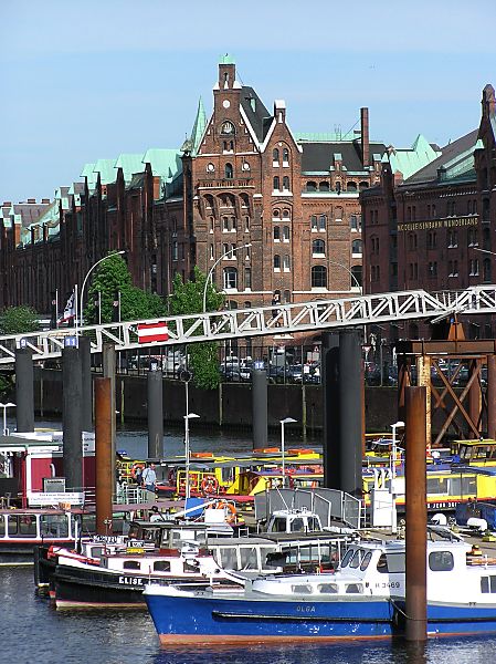 017_18959 Blick auf den Hamburger Binnenhafen; Barkassen liegen auf dem Wasser an den Dalben - im Hintergrund der Kehrwiedersteg, der zur Speicherstadt fhrt. Die kupfergedeckten Dcher der Speicherstadt schimmern in der Sonne.    www.christoph-bellin.de