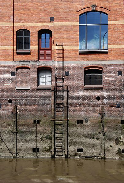 017_18961 Fassade eines Speichergebudes an der Fleetseite; es ist Ebbe - eine Leiter fhrt an der Hauswand zu einer Luke. Holzbalken die zum Schutz der Mauer vor anlegenden Schiffen angebracht wurden sind vom Zahn der Zeit zerfressen.  www.christoph-bellin.de