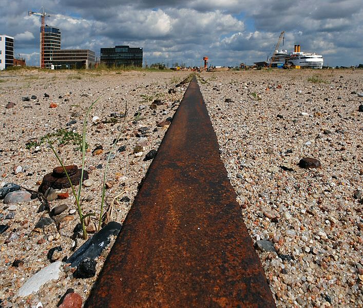 017_18963 Schiene eines ehemaligen Hafenkrans am Sandtorhafen / Grasbrookhafen - die Kaianlage ist Jahrzehnte nicht mehr genutzt worden und vom Sand zugeweht worden. Im Hintergrund in der Bildmitte der Aussichtsturm / View point von dem der Besucher der Hafencity den Fortschritt der Bauarbeiten beobachten kann; rechts das Kreuzfahrtterminal / Hamburg Cruise Center an dem ein Kreuzfahrtschiff fest gemacht hat. Links die modernen Brohuser am Grosser Grassbrook.  www.christoph-bellin.de