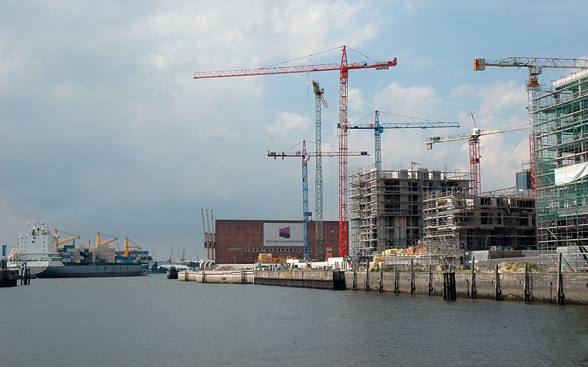 017_18971 Blick ber den Grasbrookhafen Richtung ELbe - ein Containerfrachter verlsst gerade den Hamburger Hafen und fhrt zur Nordsee; in der Bildmitte der ehem. Kaispeicher A, die zuknftige Elbphilharmonie - rechts die Baustelle (2007) der Hafencity / Kaiserkai mit den hohen Baukrnen.  www.christoph-bellin.de