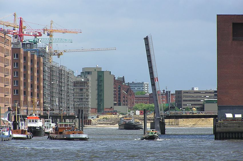 017_18975 Blick in den Sandtorhafen (2004); die Sandtorhafenbrcke ist hochgeklappt, ein Schiff fhrt aus dem Sandtorhafen zur Elbe; die Bauarbeiten am Sandtorkai sind in vollem Gange, die Baukrne stehen dicht gedrngt auf den Baustellen. Es wird am Ende des Hafenbeckens begonnen, Sand fr die zuknftigen Magellanterrassen aufzuschtten - vor dem historischen Gebude des Kaispeicher B steht noch das Gebude der Kaffeelagerei, das der Entstehung der Hafencity 2007 weichen musste.  www.christoph-bellin.de