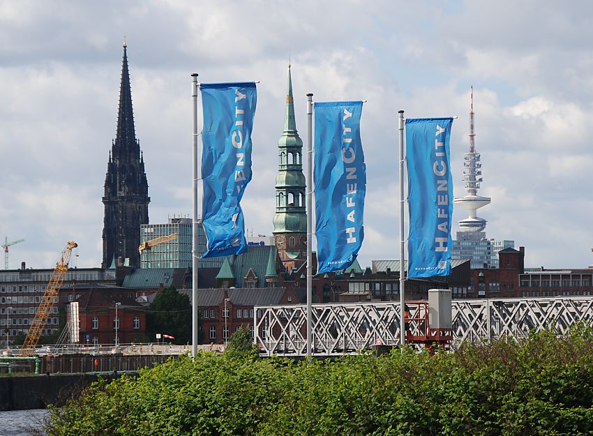 017_18988 Blick von der Elbe zur neu gebauten Baakenbrcke; die blauen Flaggen mit dem weissen Schriftzug Hafencity flattern im Wind. Im Hintergrund Turme der Stadt Hamburg: links der Kirchturm der St. Nikolaikirche, in der Mitte der Turm der Katharinenkirche und rechts der weisse Fernsehturm / Heinricht-Hertz-Turm, der im Volksmund auch Telemichel genannt wird.  www.christoph-bellin.de