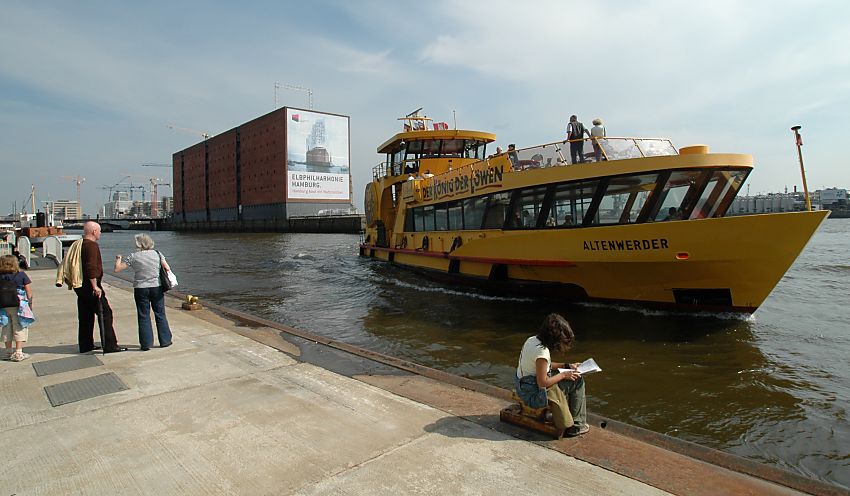 017_18997 ein Fhrschiff legt am Bootsanleger Sandtorhafen an - Fahrgste stehen und sitzen auf dem Ponton; sie warten darauf an Bord gehen zu knnen um mit der Fhre Richtung Finkenwerder fahren zu knnen.. Im Hintergrund der Kaispeicher mit seiner Werbung fr die Elbphilharmonie und die Baukrne der Hamburger Hafencity.  www.christoph-bellin.de