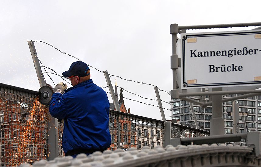 017_19000 Anfang Februar 2008 wurde begonnen, den Zollzaun am Zollkanal der Hamburger Speicherstadt zu demontieren; das Gebiet des Hamburger Freihafens wurde schon 2003 verlagert, so dass der hohe Zaun berflssig geworden ist. Hier zertrennt ein Arbeiter den Metallzaun an der Kannengiesserbrcke - die Funken sprhen. Im Hintergrund eine Skulptur auf dem Giebel eines Hauses am Zippelhaus, rechts davon ein Brogebude am Dovenfleet. www.christoph-bellin.de