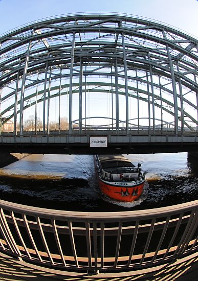 017_19016 Hamburg Fotos: im Vordergrund das Gelnder der Freihafenelbbrcke, dahinter die Eisenbahnbrcke, zwischen deren Streben der Bogen der Autobahnbrcke ber die Elbe bei Rothenburgsort zu erkennen ist. Ein rotes Binnenschiff passiert gerade die Zollgrenze auf der Elbe und fhrt in das Hamburger Freihafengebiet ein.  www.christoph-bellin.de