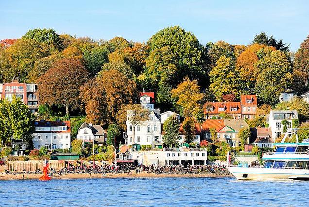 1025_1540 Herbst in Hamburg - Gste der Strandperle sitzen in der Herbstsonne am Elbstrand und geniessen den Ausblick. Die Bume am Elbhang leuchten in ihren prchtigen Herbstfarben. Ein Fahrgastschiff einer Hafenrundfahrt fhrt auf seiner Tour durch den Hamburger Hafen entlang der Elbe.