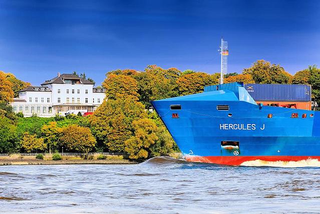 1033_0692 Das Feederschiff HERCULES J luft aus dem Hamburger Hafen aus und fhrt elbabwrts; im Hintergrund der bewaldete Elbhang mit herbstlich gefrbten Laubbumen. Eine weisse Villa steht mit Blick auf die Elbe steht zwischen den Bumen. 