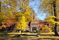1611_1730 Die Herbstsonne scheint auf die Herbstbume, die beim historischen Torhaus von Hamburg Wellingsbtel stehen. Der Rasen vor dem historischen Gebude ist mit gelben Blttern bedeckt; ein Passant geht auf dem Kopfsteinpflaster zum Fachwerkgebude des 1757 errichteten Torhauses. 