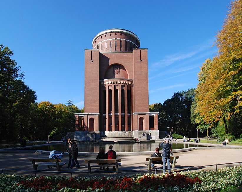 16_03795 Herbst im Hamburger Stadtpark - das Laub der Bume am Winterhuder Planetarium sind herbstlich gefrbt. Besucher des Parks sitzen in der Herbstsonne auf Bnken oder am Rand des Wasserbassins - ein Fotograf fotografiert das historische Gebude des Planetarium. Im Vordergrund eine bunte Blumenrabatte.   www.christoph-bellin.de