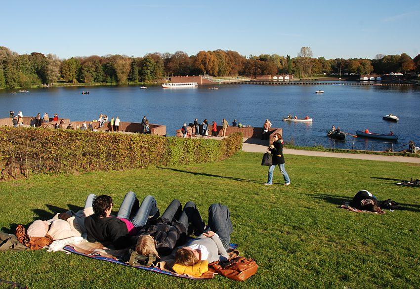 16_03810 Stadtparkbesucher und Besucherinnen geniessen am Sonntag-Nachmittag die letzten warmen Strahlen der Herbstsonne auf der Wiese am Stadtparksee. Einige liegen warm angezogen auf einer Decke im Gras andere wrmen sich in der Sonne an der Ziegelmauer der Kaskaden.   www.christoph-bellin.de