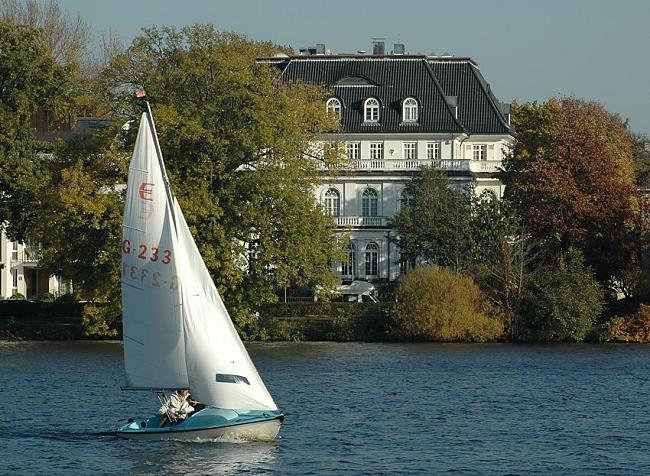 16_03828 Blick zur Strasse Bellevue in Hamburg Winterhude - eine weisse Stadtvilla steht zwischen herbstlich gefrbten Bumen und Bschen am Alsterufer. Im Vordergrund ein Segelboot im Wind auf dem Wasser der Alster.  www.christoph-bellin.de