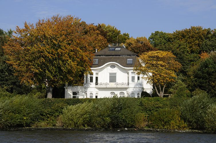 16_038163 weisse Jugendstilvilla an der Elbchaussee mit Blick auf die Elbe - die Villa steht inmitten von hohen Bumen, die ihre rote und gelbe Herbstfrbung angenommen haben. Am Elbufer haben die Bltter der Weiden noch ein frisches Grn.  www.christoph-bellin.de