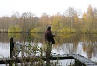 1717_2490 Ein Angler steht mit seiner auf einem Holzsteg am Ufer des Rckhaltebeckens bei den Teichwiesen von Hamburg Volksdorf - ein grosser Ketscher, mit dem der Fang an Land geholt werden soll, lehnt an einem Balken. Am gegenber liegenden Ufer stehen Bume mit herbstlich gefrbten Blttern; teilweise ragen Strucher und Zweige weit ber das Wasser.