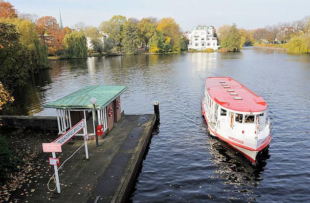 343_0699 IDas Fahrgastschiff Ammersbek der weissen Alsterflotte hat hinter der Krugkoppelbrcke gewendet und passiert den Schiffsanleger / Haltestelle Krugkoppelbrcke. Im Hintergrund lks. Bume am Wasser des Eichenparks von Hamburg Harvestehude und Bume im Herbstgewand am Ufer der Alster.  