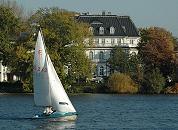 16_03828  Blick zur Strasse Bellevue in Hamburg Winterhude - eine weisse Stadtvilla steht zwischen herbstlich gefrbten Bumen und Bschen am Alsterufer. Im Vordergrund ein Segelboot im Wind auf dem Wasser der Alster.  www.christoph-bellin.de