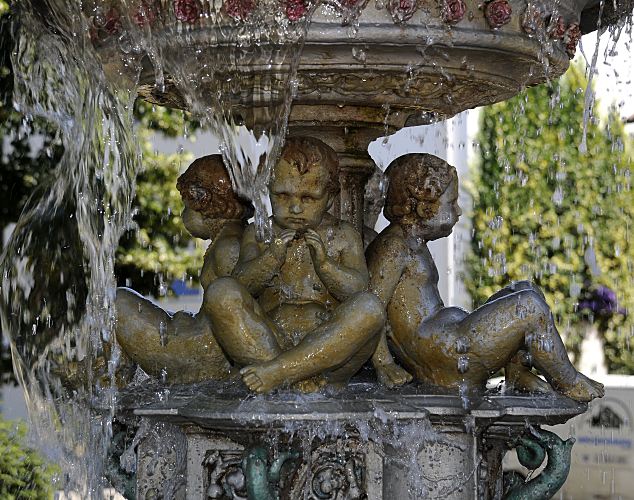 Zwischen dem kleinen und grossen Becken vom gusseisernen Sievers Brunnen sitzen vier Putten unter dem rinnenden Wasser.  Abbildung der Putten am Sievers Brunnen in Hamburg Bergedorf