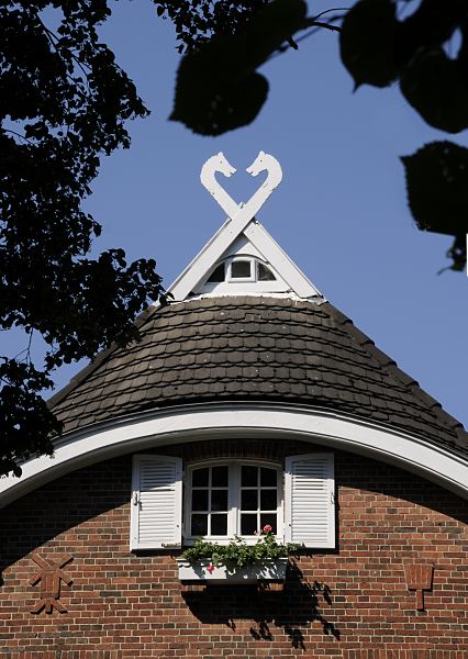 Architekturbilder aus Hamburg Bergedorf Fachwerkhaus im Bergedorfer Villenviertel; zwei Pferdekpfe sind auf dem Dach des Hauses als Giebelschmuck angebracht. Im Klinker-Mauerwerk sind mit Steinen Dekore u.a. eine Mhle und ein Besen? gemauert. Vor dem Giebelfenster mit zwei Holzluken hngt ein Blumenkasten mit Geranien. Ende des 19.  Jahrhunderts wurde begonnen, im sogenannte Villenviertel zu bauen -  wohlhabende Hamburger und Bergedorfer Brger lieen dort ihre reprsentativen Wohnhuser errichten. Es entstanden Stadthuser, die die unterschiedlichen Stile der Architektur ausdrcken - neben der Bauform der Grnderzeit wurde auch der Jugendstil architektonisch umgesetzt oder Wohnhuser in der Architektur der neuen Sachlichkeit gebaut.