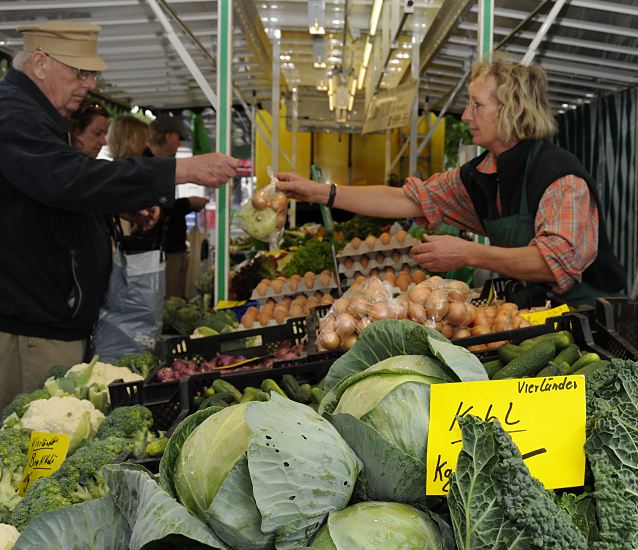 Hamburger Wochenmarkt in Lohbrgge, Bezirk Bergedorf - Vierlnder Kohl  - An dem Gemsestand vom Wochenmarkt in Hamburg Bergedorf / Stadtteil Lohbrgge wird frischer Vierlnder Kohl verkauft - im Vordergrund liegen grosse Kohlkpfe Weisskohl, daneben die typischen Kohlbltter vom Wirsingkohl -  auf der linken Seite liegen der Brokkoli und der Blumenkohl. Dahinter sind Kisten mit Zwiebeln und Pappkartons mit frischen Eiern. Die Markthndlerin reicht dem Kunden seinen Einkauf, er gibt ihr das Geld fr das gekaufte Gemse.