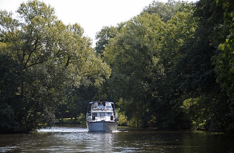 der Hamburger Bezirk Bergedorf in Fotos - Motoryacht auf der Doveelbe.  Eine weisse Motoryacht fhrt flussabwrts auf der Dove-Elbe; hohe Bume stehen am Flussufer, die ste wachsen bis zur Mitte des Flusse und bilden fast ein grnes Dach.