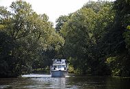 17_21581 Eine weisse Motoryacht fährt flussabwärts auf der Dove-Elbe; hohe Bäume stehen am Flussufer, die Äste wachsen bis zur Mitte des Flusse und bilden fast ein grünes Dach. ©www.hamburg-fotograf.com