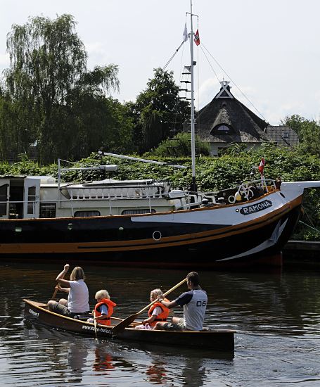 Hamburger Fotografien - Sommer in Hamburg Bergedorf   Eine Familie paddeln in einem Kanu auf der Dove-Elbe - die Kinder tragen zur Sicherheit Schwimmwesten. Am Ufer liegt ein Segelschiff, das zum Hausboot umgebaut wurde, dahinter ein strohgedecktes Wohnhaus.