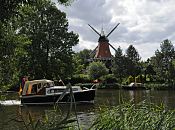 17_21593 Die Dove-Elbe ist ein beliebtes Hamburger Gewsser fr Freizeitkapitne. Ein Motorboot fhrt flussabwrts, am Bug fhrt es die Hamburg-Fahne und am Heck die Deutschlandflagge. Die kleine Motoryacht passiert gerade die historische Reitbrooker Windmhle. Die Kornmhle wurde  ursprnglich 1773 errichtet und nach einem Brand 1870 neu erbaut. Am Ufer im Vordergrund wchst dichtes Schilf - auf der anderen Uferseite liegt am Bootsanleger ein kleines Sportboot. www.hamburg-fotograf.com