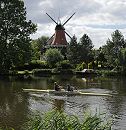 17_21594 Die Dove-Elbe ist ein beliebtes Hamburger Gewsser fr Freizeitkapitne. Ein Motorboot fhrt flussabwrts, am Bug fhrt es die Hamburg-Fahne und am Heck die Deutschlandflagge. Die kleine Motoryacht passiert gerade die historische Reitbrooker Windmhle. Die Kornmhle wurde  ursprnglich 1773 errichtet und nach einem Brand 1870 neu erbaut. Am Ufer im Vordergrund wchst dichtes Schilf - auf der anderen Uferseite liegt am Bootsanleger ein kleines Sportboot. www.hamburg-fotograf.com