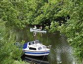 17_21604 Blick auf die Dove-Elbe bei Hamburg Reitbrook; das Ufer des Flusses ist dicht mit hohen Bumen bewachsen - die ste hngen dicht ber dem Wasser. Ein Kanu fhrt auf dem ruhigen Wasser der Doeveelbe, im Vordergrund ist ein kleines Motor-Sportboot am Bootssteg vertut. www.hamburg-fotograf.com